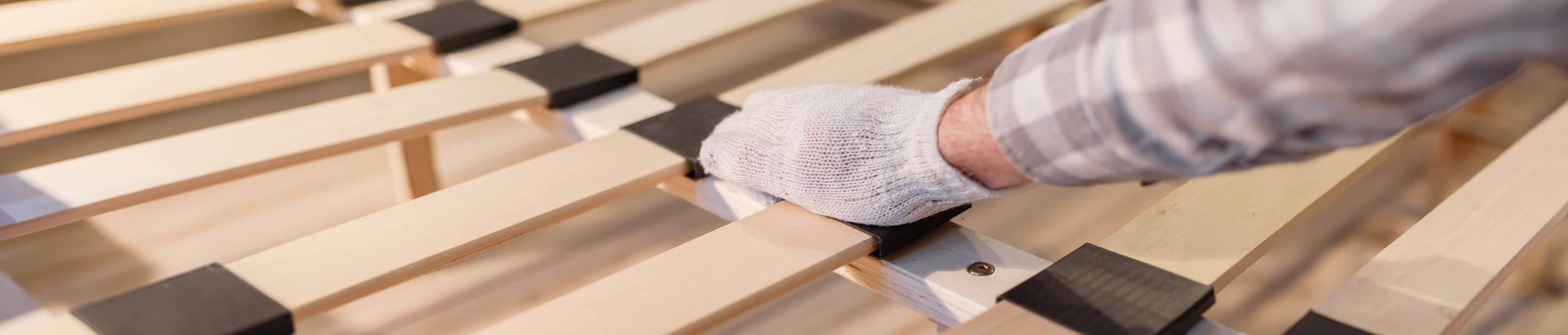 Mann fasst mit einem Handschuh den Lattenrost an.